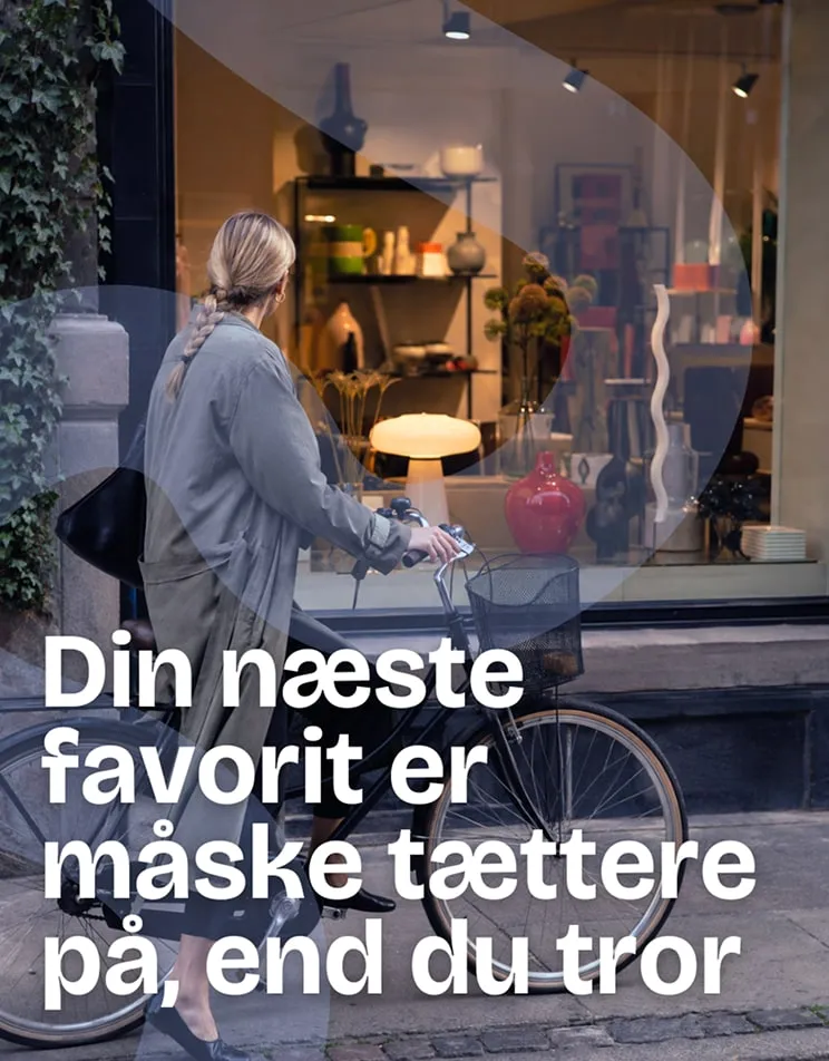 Kvinde med cykel foran et butiksvindue. Tekst: Din næste favorit er måske tættere på, end du tror.