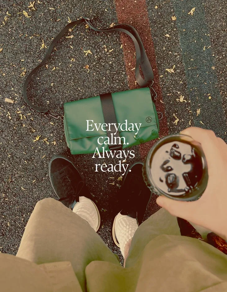 Grøn KIWEE-taske på asfalt set oppefra. Tekst: Everyday calm. Always ready.
